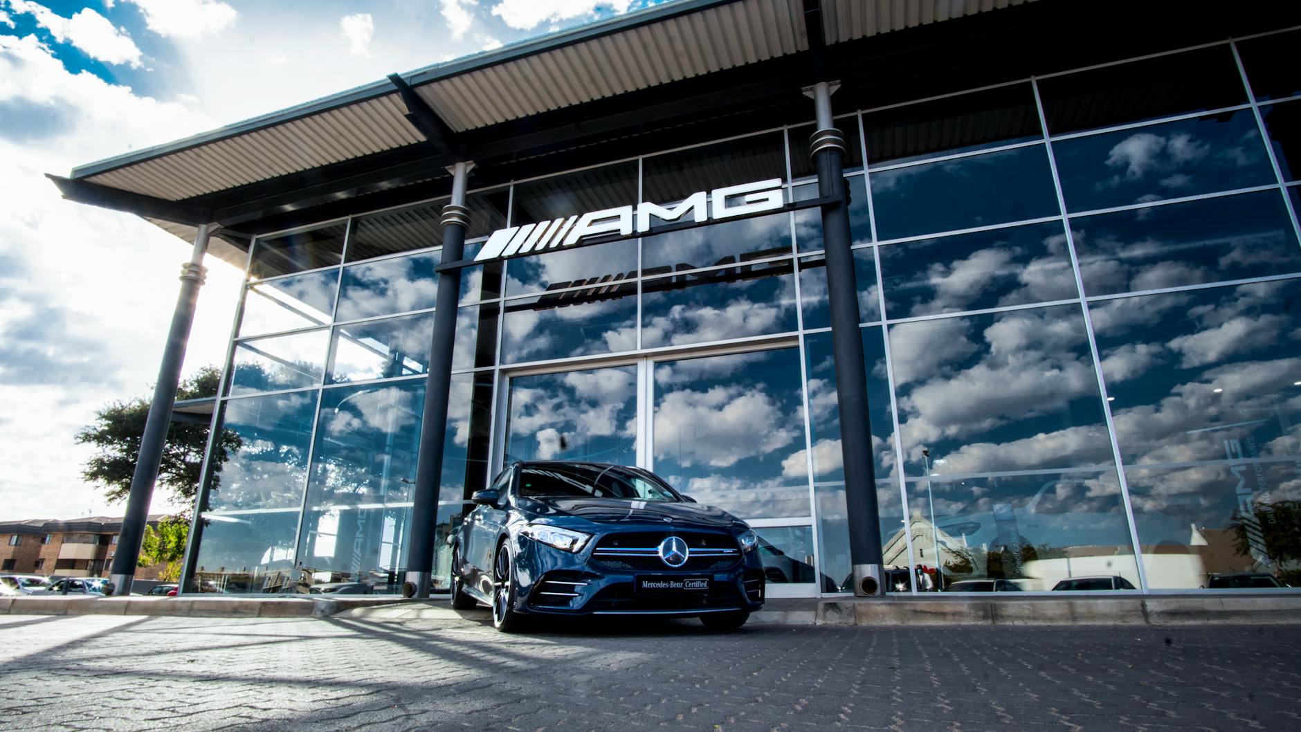 Niebieski Mercedes-Benz przed salonem AMG na tle pochmurnego nieba