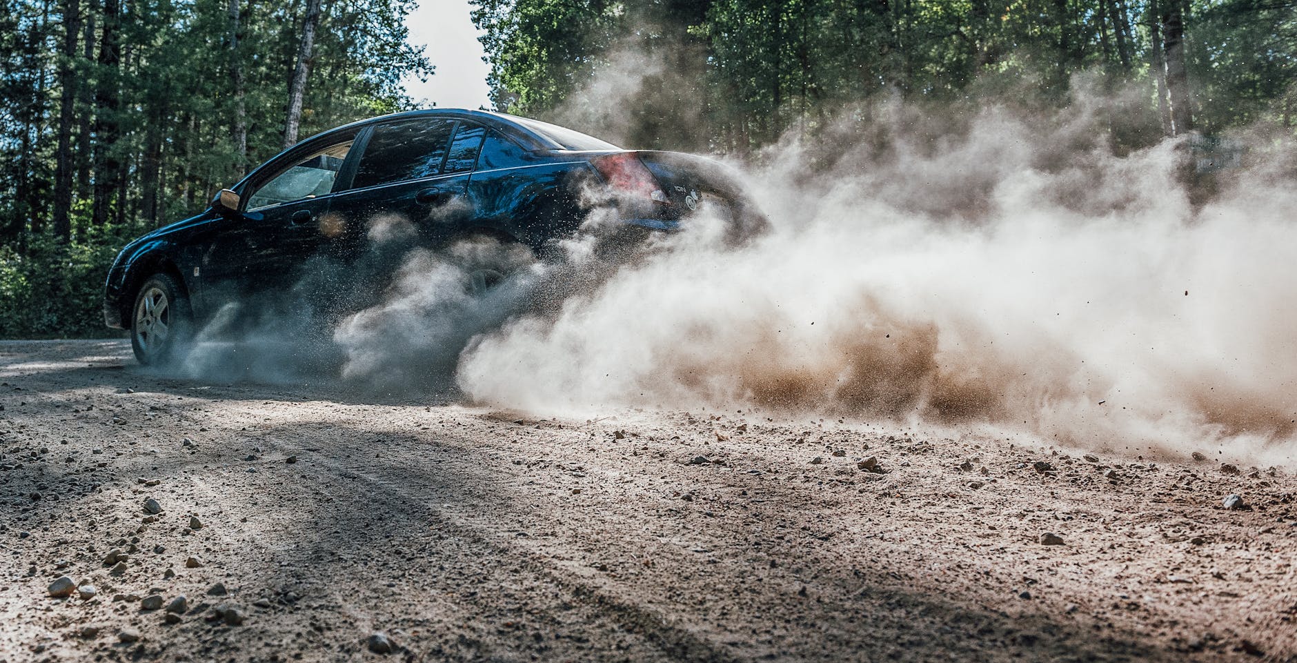 Rajdowe auto pędzi leśną drogą, wzbijając chmurę kurzu