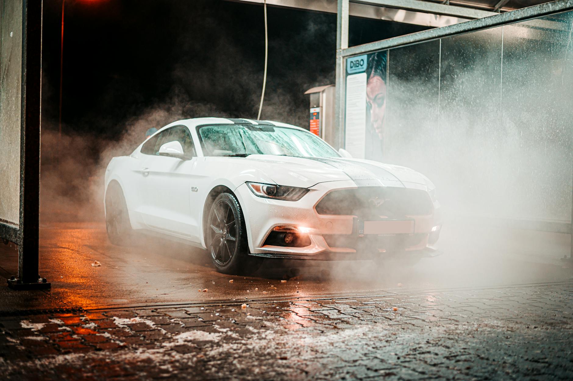 Białe coupe Ford Mustang nocą w miejskiej myjni w lekkiej mgle