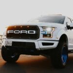 Range Rover vs BMW X7: który lepszy na trasę? Biały SUV jedzie nadmorską trasą o zachodzie słońca