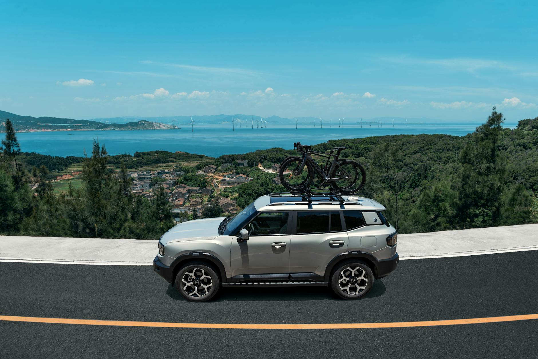 Srebrny SUV Discovery Sport z rowerami na dachu na nadmorskiej drodze