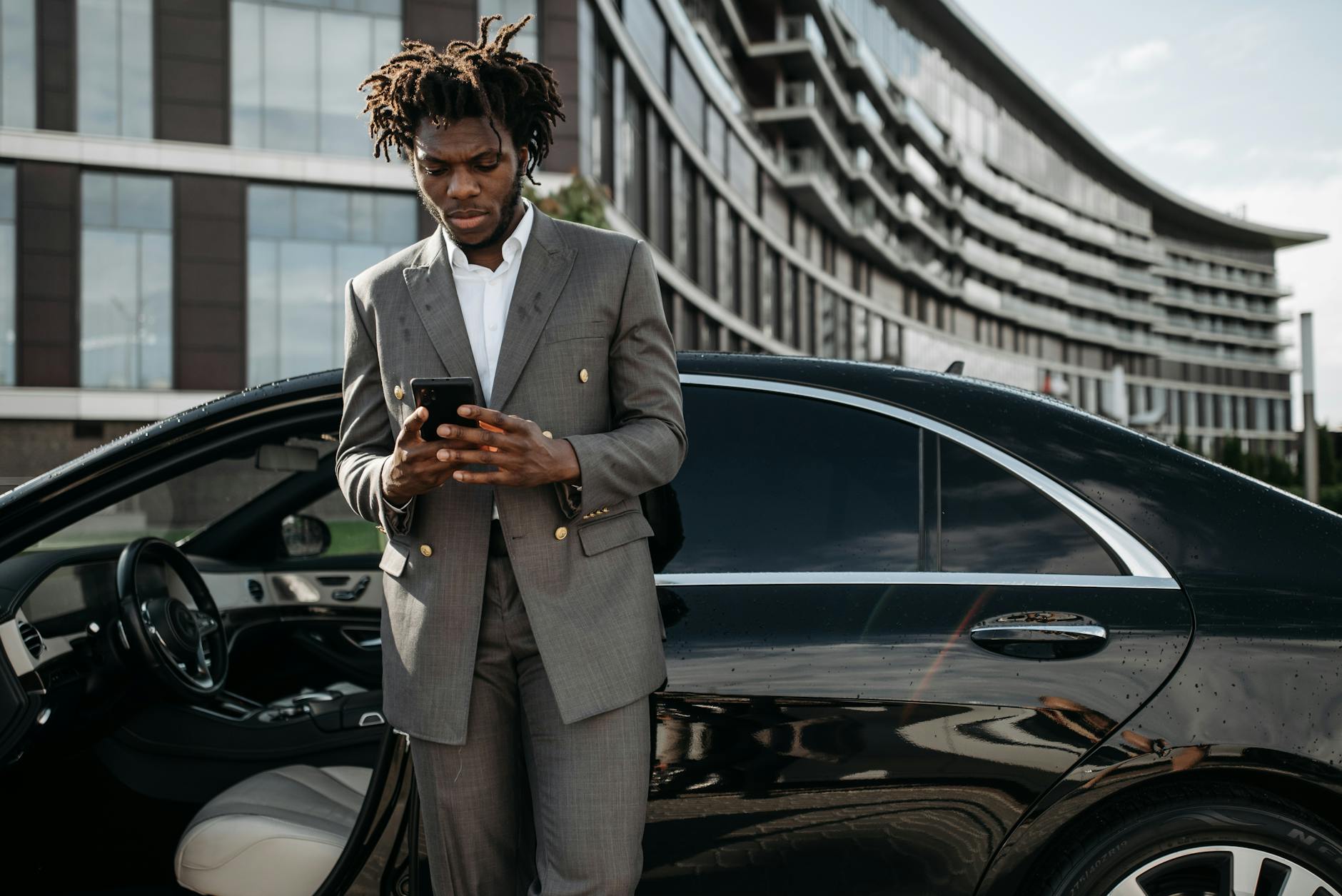 Elegancki mężczyzna w garniturze korzysta ze smartfona przy aucie premium