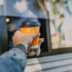 Kierowca odbiera kubek kawy z okienka kawiarni drive-thru