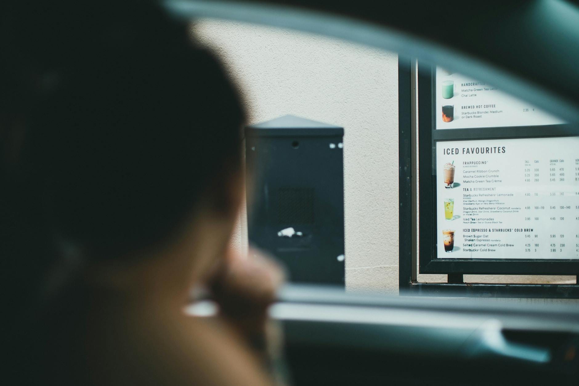 Kierowca zamawia kawę przy okienku drive-thru, menu w tle