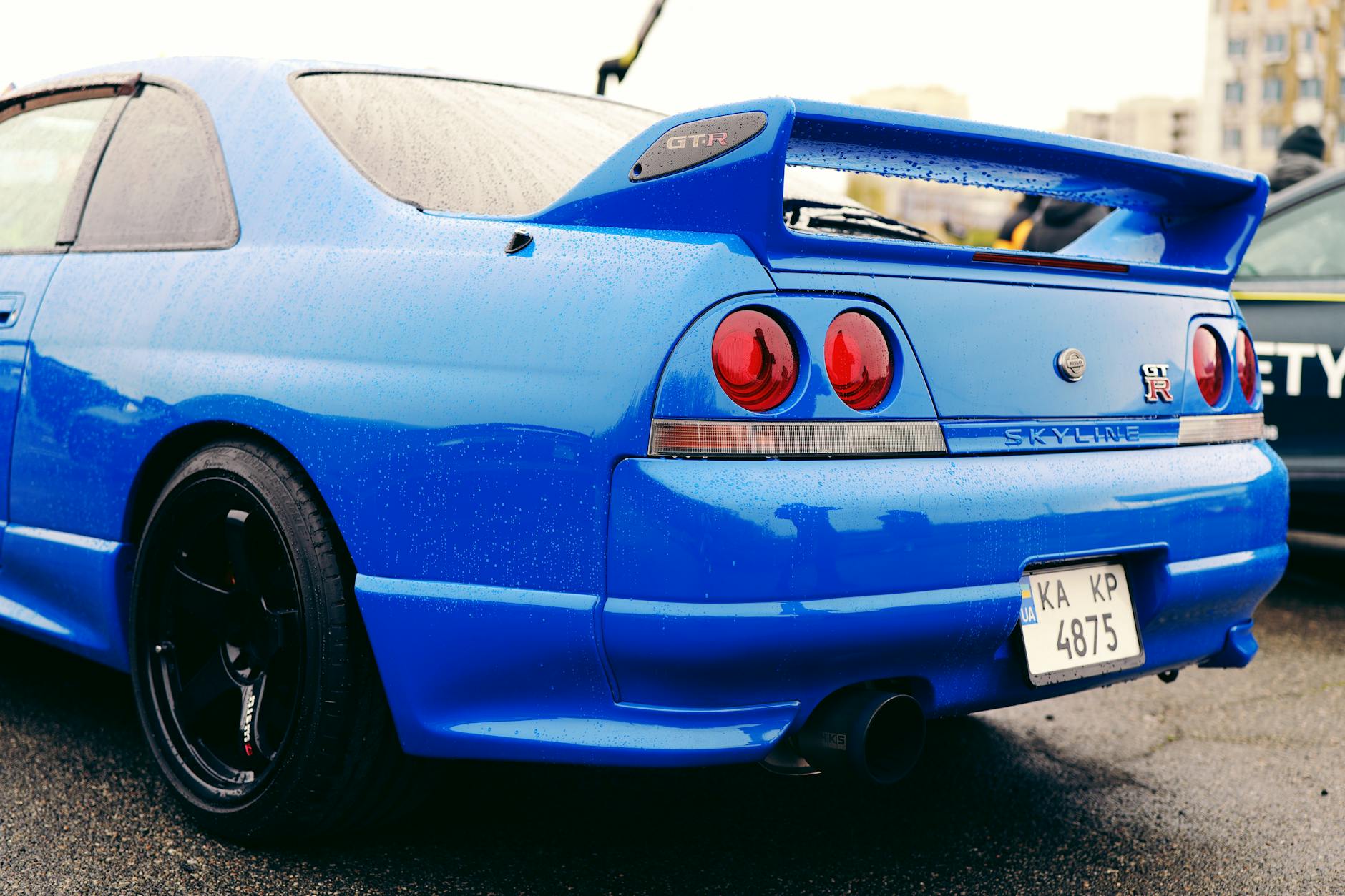 Niebieski Nissan Skyline GT-R na mokrym parkingu podczas zlotu aut