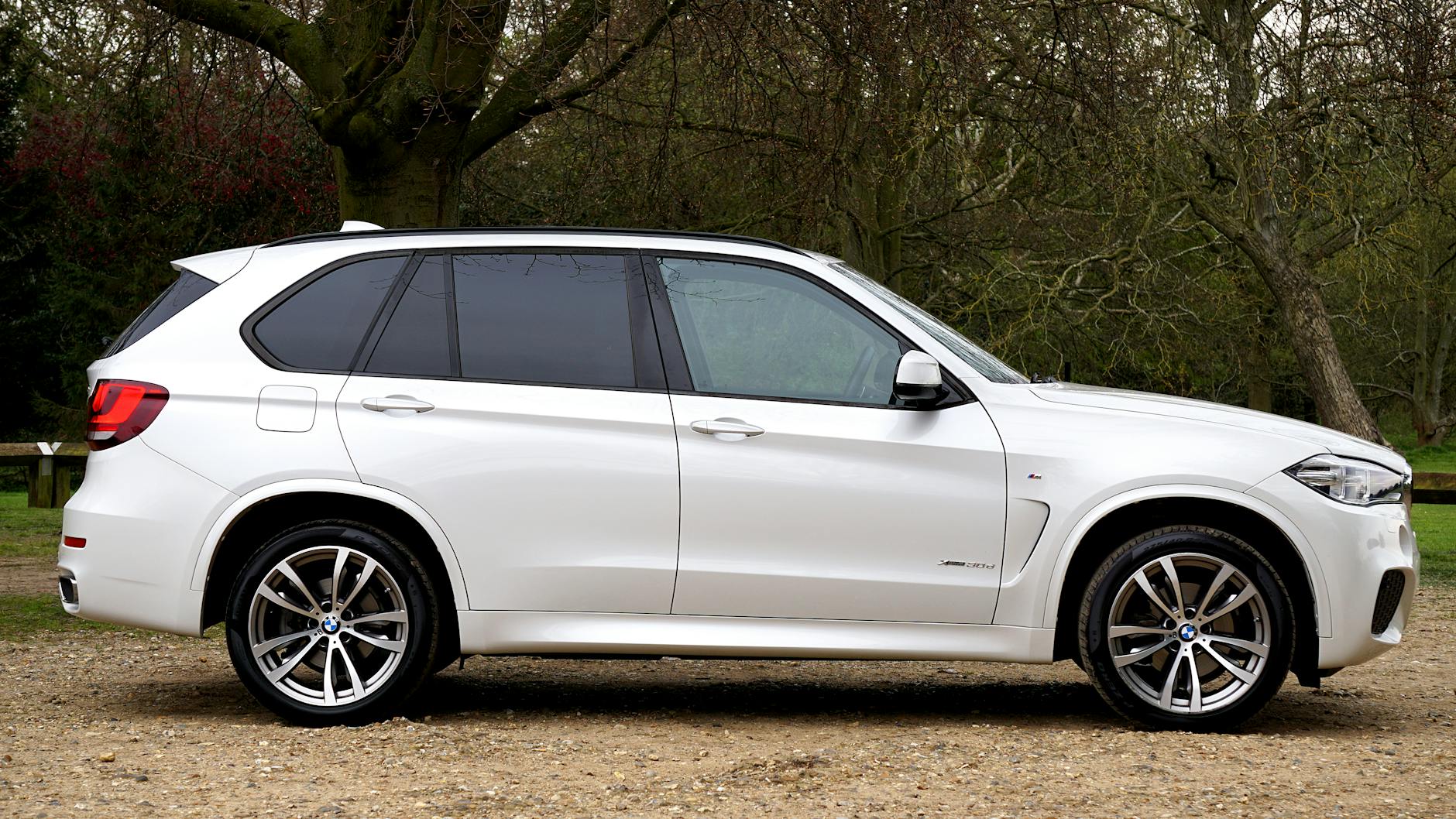 Białe luksusowe BMW SUV zaparkowane na żwirowej drodze w zielonym otoczeniu Białe luksusowe BMW SUV zaparkowane na żwirowej drodze w zielonym otoczeniu
