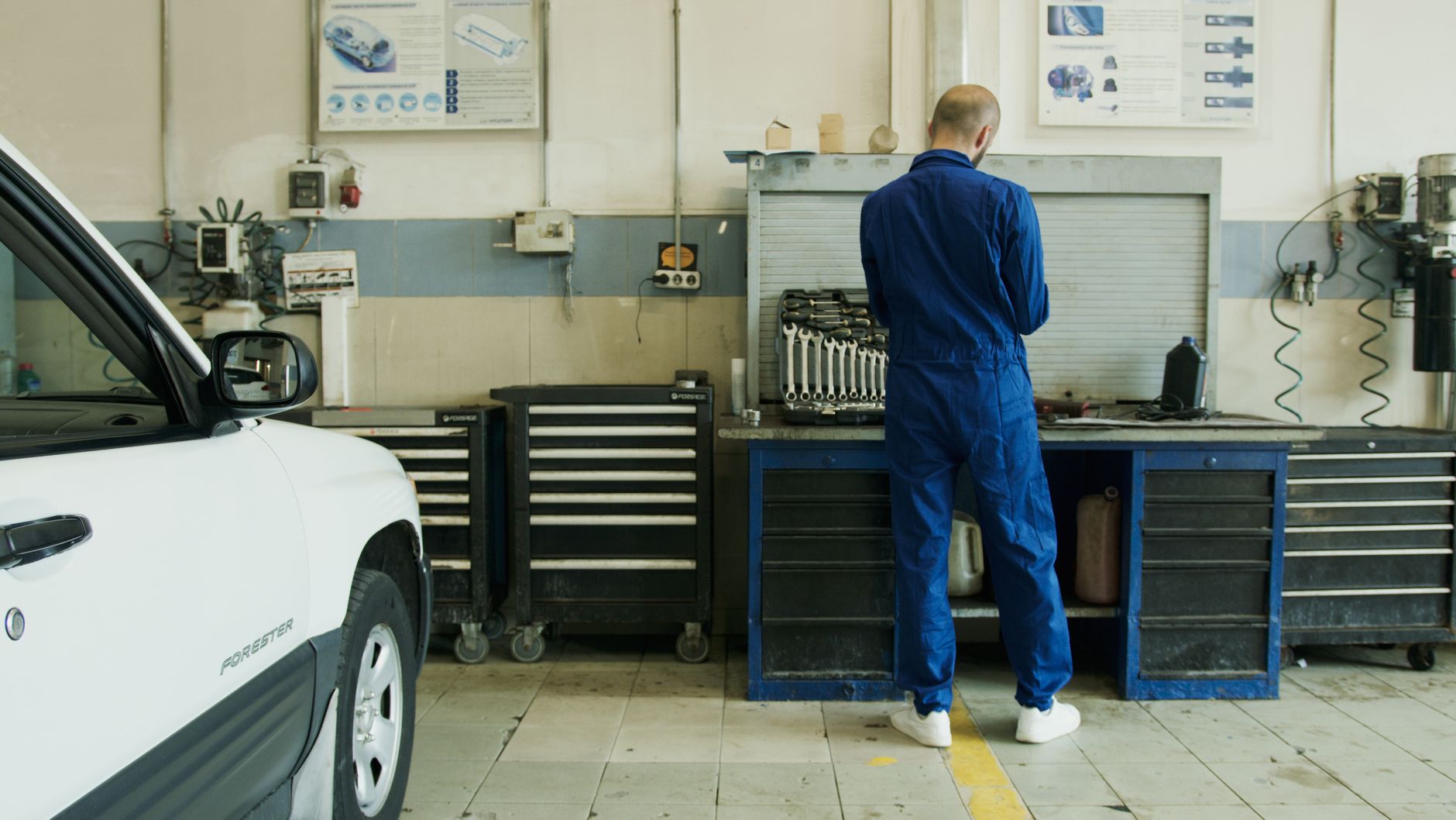 Mechanik w niebieskim kombinezonie sprawdza biały samochód w warsztacie